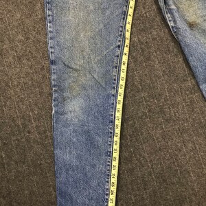 May include: Light blue denim jeans with a measuring tape alongside the leg. The tape indicates a length of approximately 79 cm. The jeans have a classic five-pocket design and a faded wash.