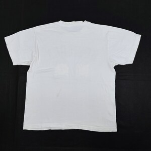 Puede incluir: Una camiseta blanca lisa, vista desde la espalda, con mangas cortas y cuello redondo. La camiseta est&aacute; hecha de una tela suave y opaca y est&aacute; colocada sobre una superficie negra. La apariencia general es simple y casual.