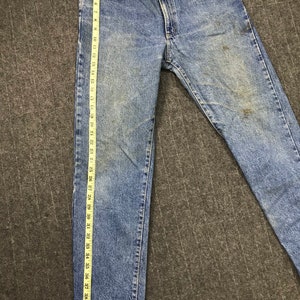 May include: Light blue denim jeans with a straight leg cut. The jeans are measured with a ruler, showing a length of approximately 104 cm. The denim has a faded wash and some discoloration.