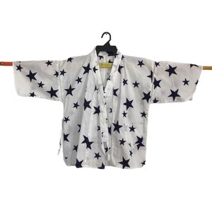 May include: White cotton kimono with a navy blue star pattern. The kimono has a tie closure and is hanging on a black hanger.