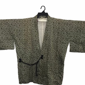 Puede incluir: Un kimono japonés tradicional con un patrón geométrico en tonos verdes y blancos. El kimono tiene una corbata negra y está colgado en una percha.