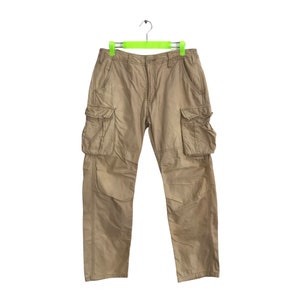 Könnte beinhalten: Eine Khaki-Cargohose mit mehreren Taschen, die an einem grünen Kleiderbügel hängt.