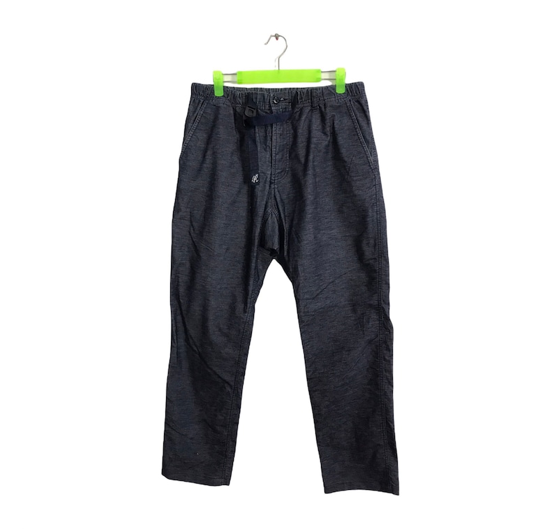 Op de afbeelding: Donkerblauwe spijkerbroek hangt aan een groene hanger. De broek heeft een taille met trekkoord en een klein logo aan de voorkant. De stof lijkt een mediumgewicht denim te zijn. De broek heeft een relaxte pasvorm.