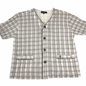 May include: A short-sleeved, button-down shirt with a plaid pattern in shades of gray and white. The shirt has a V-neck, two front pockets, and black trim. The buttons are dark gray.