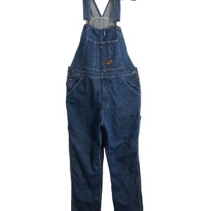 May include: Blue denim overalls with adjustable straps and multiple pockets. The overalls are hanging on a black hanger. The garment features a chest pocket and a small logo patch. The overall length is approximately 152 cm.