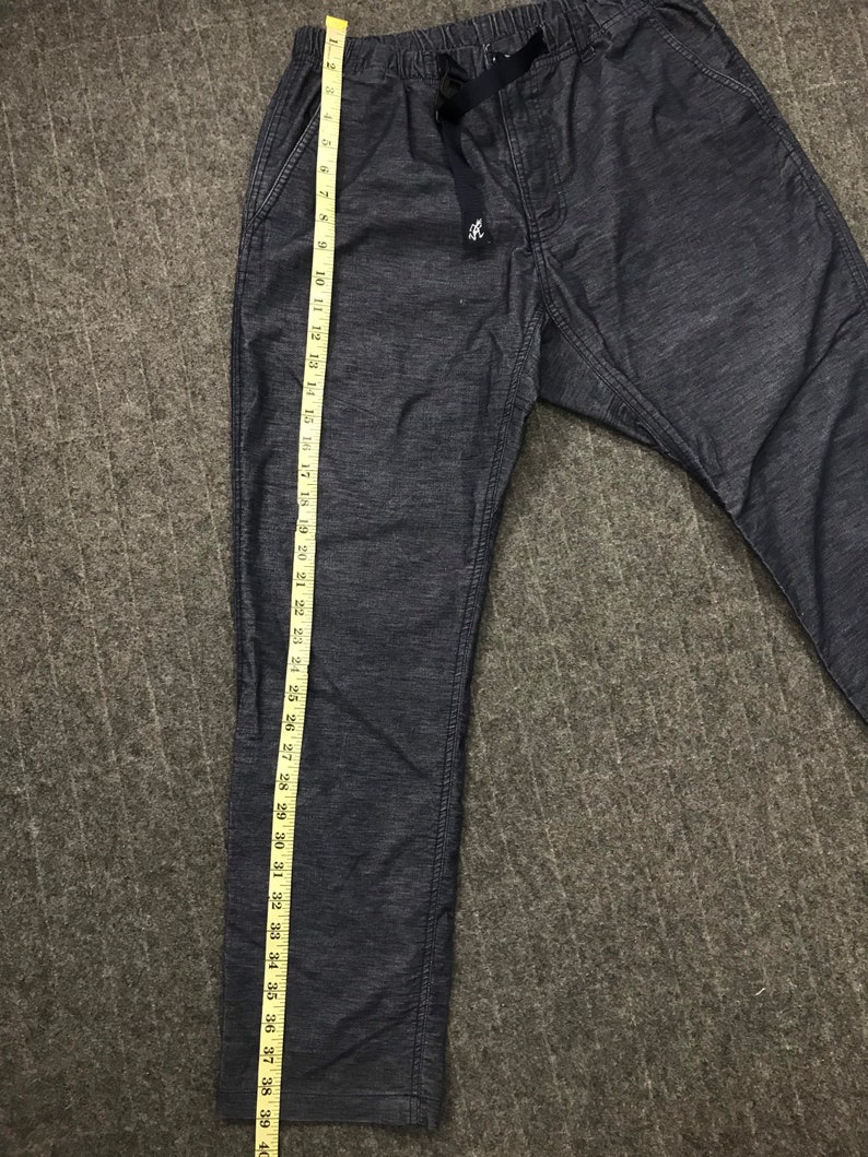 Op de afbeelding: Donkerblauwe vrijetijdsbroek met een tailleband met trekkoord en zijzakken. De broek wordt gemeten met een gele meetlint, met een lengte van ongeveer 99 cm. De stof heeft een subtiel textuurpatroon.