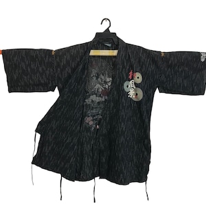 May include: Black kimono-style jacket with white vertical stripe pattern. The jacket features a graphic design on the inside and Japanese text and imagery on the front. The sleeves are wide and the jacket is open in the front.