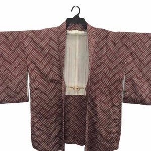 May include: A brown and white patterned Japanese kimono with a geometric design. The kimono is hanging on a black hanger.