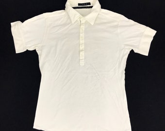 May include: A white short-sleeved shirt with a collared neckline and a button-down placket. The shirt has rolled-up sleeves and the text "A.A.P." is visible on the collar.