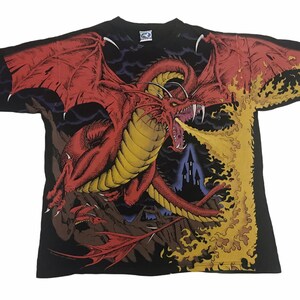 May include: Black t-shirt featuring a detailed illustration of a red dragon breathing fire. The dragon has large wings and sharp teeth. The background includes a castle silhouette and flames.