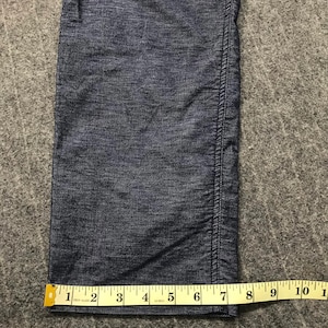 Op de afbeelding: Close-up van een donkerblauwe spijkerbroek met een gele meetlint. De tape toont een meting van ongeveer 15 cm. De jeans heeft een zichtbare naad aan de rechterkant.