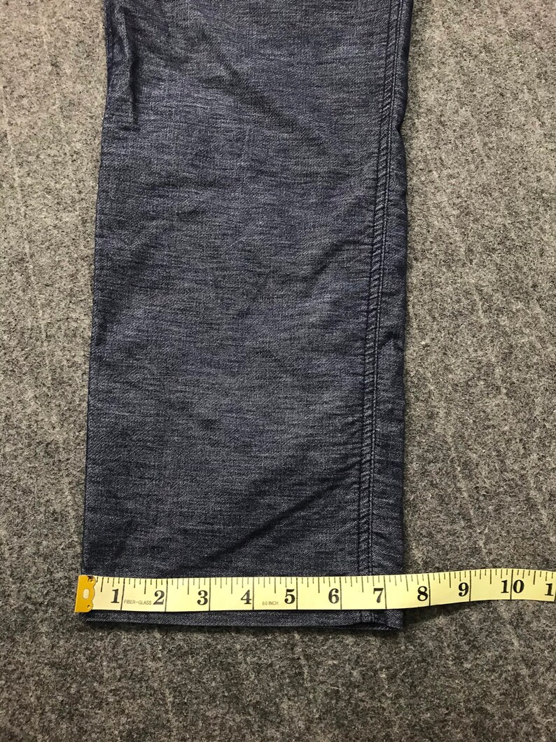 Op de afbeelding: Close-up van een donkerblauwe spijkerbroek met een gele meetlint. De tape toont een meting van ongeveer 15 cm. De jeans heeft een zichtbare naad aan de rechterkant.