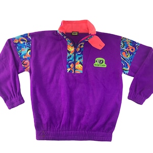 May include: A purple fleece pullover with a coral collar and patterned accents on the shoulders and zipper. The pullover features a zip closure, elastic cuffs, and a waist. The logo "YACH CLUB" is on the chest.