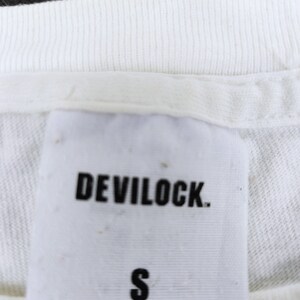 Puede incluir: Primer plano de una etiqueta de camiseta blanca con el nombre de la marca "DEVILOCK" en letras negras en negrita. Debajo del nombre de la marca est&aacute; la letra "S" en negro. La parte inferior de la etiqueta tiene texto que es dif&iacute;cil de leer.