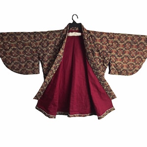 May include: A traditional Japanese kimono. The outer fabric features a pattern in brown, beige, and red. The interior lining is a solid burgundy colour. The kimono is open, showing the lining and the detailed design.