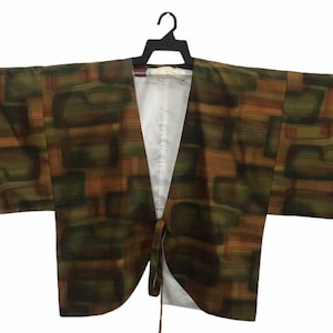 Puede incluir: Un kimono estampado en marrón y verde con cierre de nudo. El kimono tiene cuello en V y está hecho de una tela suave y ligera.