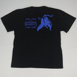May include: Black t-shirt with a blue graphic on the back. The graphic includes the text "SENGOKU BASARA 3" and two stylized figures in action poses. The shirt is a crew neck style.