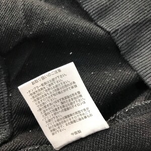 May include: Close-up of a black fabric with a white tag attached. The tag has Japanese text and care instructions. The fabric appears to be a dark, textured material, possibly a sweatshirt or similar garment.
