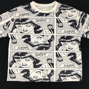 May include: A white t-shirt with a black and grey comic strip design. The print shows panels with a crying woman and the text "OH GOD! WHY CAN'T MY BOYFRIEND SKATE?!" A man in a suit is also featured in the design.