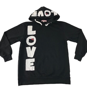 May include: Black hooded sweatshirt with the word "LOVE" in large white letters down the front. The hood features the word "LOVE" in white. A small Hello Kitty graphic is incorporated into the "O" in "LOVE".