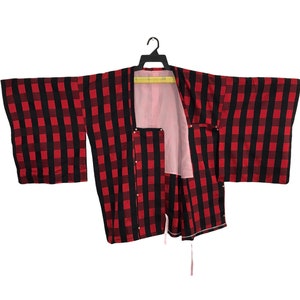 May include: A red and black checked kimono with a pink lining. The kimono is hanging on a wooden hanger.