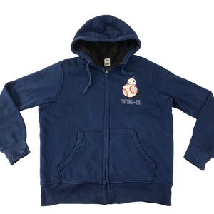Puede incluir: Sudadera con capucha azul marino con cremallera y gráfico de BB-8 de Star Wars. Tiene capucha con cordón, bolsillo tipo canguro y puños acanalados. El forro interior es de un material oscuro y difuso.
