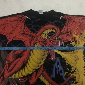 May include: Black t-shirt featuring a detailed red dragon graphic with large wings, spewing flames. The dragon is set against a dark background with a castle silhouette. The shirt's design covers the entire front.
