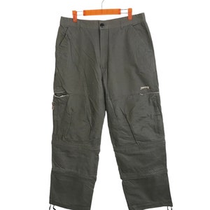 Könnte beinhalten: Grüne Cargohose mit mehreren Taschen und einem Kordelzug am unteren Ende. Die Hose hat den Schriftzug "Timberland" auf dem rechten Bein.