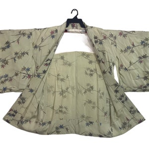 May include: A green kimono with a floral pattern. The kimono is open and the sleeves are folded back. The kimono is made of a lightweight fabric and has a relaxed fit.