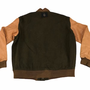May include: A dark green varsity jacket with brown leather sleeves. The jacket has a brown ribbed collar, cuffs, and waistband. There is a small logo patch on the back of the jacket.