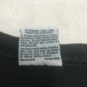 May include: Close-up of a black garment with a white tag attached. The tag contains care instructions, including washing and drying instructions, and the text "TO ENSURE LONG LIFE FROM THIS GARMENT:" and the numbers "RN13765" and "RN 81758".