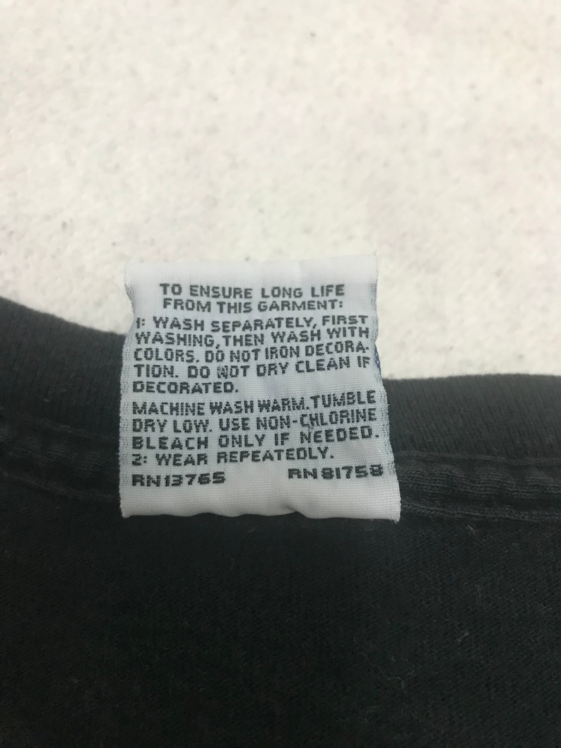 May include: Close-up of a black garment with a white tag attached. The tag contains care instructions, including washing and drying instructions, and the text "TO ENSURE LONG LIFE FROM THIS GARMENT:" and the numbers "RN13765" and "RN 81758".