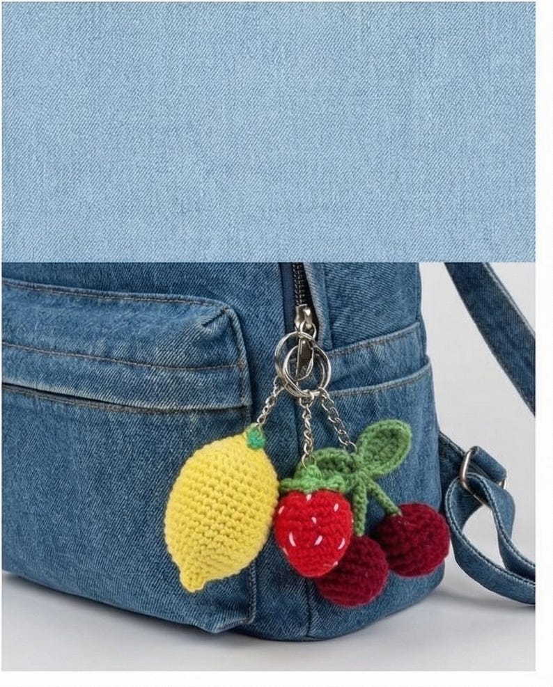 Peut inclure: Un sac &agrave; dos en jean bleu avec une poche avant et une fermeture &eacute;clair argent&eacute;e. Le sac &agrave; dos est orn&eacute; d'un porte-cl&eacute;s avec des breloques de fruits crochet&eacute;s : un citron jaune, une fraise rouge et deux cerises marron.