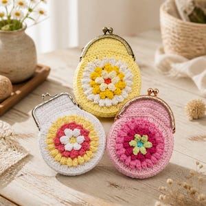 Puede incluir: Tres monederos redondos de ganchillo con cierres metálicos de presión. Un monedero es amarillo con un patrón de flores blancas y amarillas, otro es blanco con una flor amarilla, rosa y blanca, y otro es rosa con una flor rosa oscuro y verde claro.