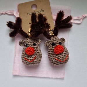 K&ouml;nnte beinhalten: Ein Paar handgefertigte geh&auml;kelte Rentierohrringe mit braunen Geweihen und roten Nasen. Die Ohrringe sind in einem rosa Organzas&auml;ckchen mit einem braunen Etikett verpackt, auf dem "Handmade" steht.