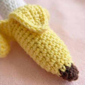May include: A handmade crochet banana in shades of yellow and brown. The banana peel is a bright yellow, with a textured surface. The tip of the banana is brown. The banana is partially peeled, revealing a white interior.