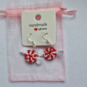 K&ouml;nnte beinhalten: Geh&auml;kelte Zuckerstangen-Ohrringe mit silbernen Haken. Die Ohrringe sind in einem rosa Organzas&auml;ckchen mit einem wei&szlig;en Etikett verpackt, auf dem "Handmade with love" steht.