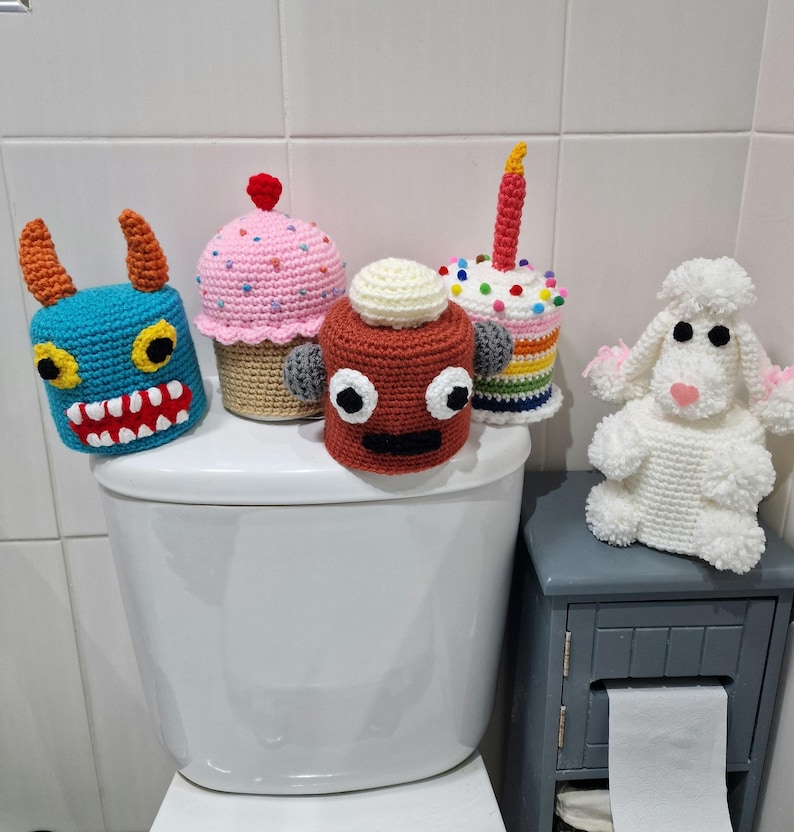 Puede incluir: Una colecci&oacute;n de cubiertas de rollo de papel higi&eacute;nico de ganchillo caprichosas y una peque&ntilde;a figura de cordero. Las cubiertas incluyen un monstruo azul, una magdalena rosa, un robot rojo, una tarta de cumplea&ntilde;os y un cordero blanco con acentos rosas.