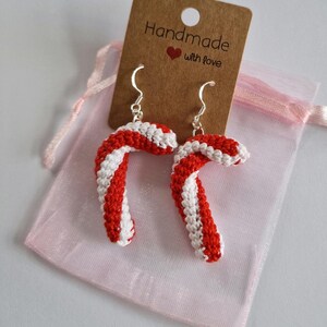 K&ouml;nnte beinhalten: Ein Paar rote und wei&szlig;e Zuckerstangen-Ohrringe mit silbernen Haken. Die Ohrringe sind handgefertigt und werden mit einem kleinen braunen Etikett geliefert, auf dem "Handmade with love" steht.