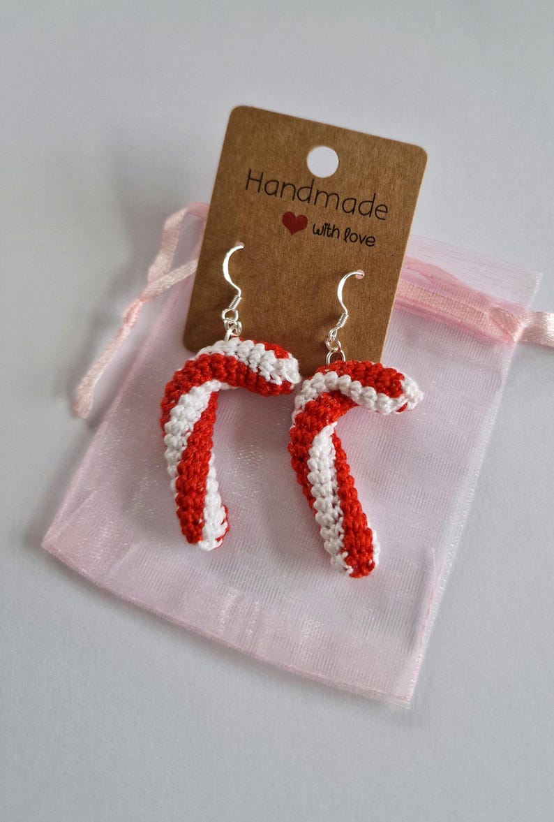 K&ouml;nnte beinhalten: Ein Paar rote und wei&szlig;e Zuckerstangen-Ohrringe mit silbernen Haken. Die Ohrringe sind handgefertigt und werden mit einem kleinen braunen Etikett geliefert, auf dem "Handmade with love" steht.