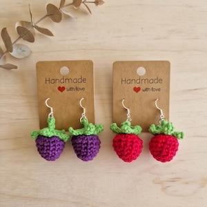 May include: Two pairs of crochet fruit earrings on brown cardboard display cards labeled Handmade with love. One pair features purple berries with green tops, and the other pair features red berries with green tops, all attached to silver-toned metal hooks.