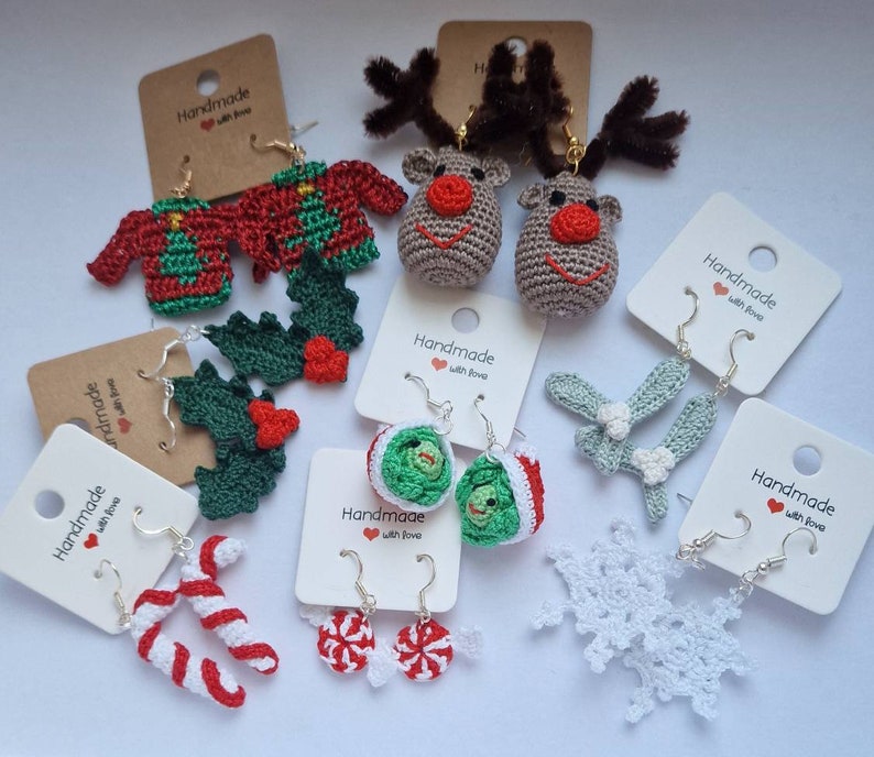 K&ouml;nnte beinhalten: Eine Auswahl an handgefertigten Ohrringen zum Thema Weihnachten. Die Ohrringe sind aus geh&auml;keltem Garn gefertigt und zeigen verschiedene Designs, darunter Rentiere, Stechpalmen, Zuckerstangen, Schneeflocken und Weihnachtspullover. Die Ohrringe werden auf wei&szlig;en Karten mit dem Text "Handmade with love" pr&auml;sentiert.