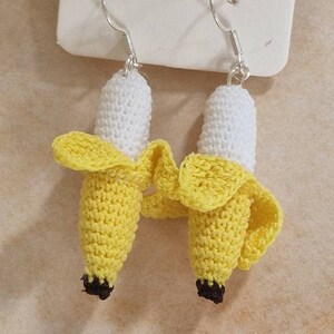 Handmade crocheted banana earrings.  The earrings are yellow and white, with silver hooks. The packaging shows the words 'Handmade with love'. These charming, whimsical earrings are perfect for adding a touch of fun to any outfit.