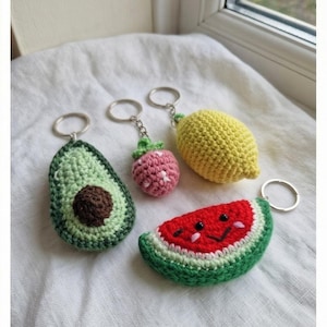 Peut inclure: Une collection de porte-cl&eacute;s crochet&eacute;s &agrave; la main en forme de fruits. Comprend un avocat, une fraise, un citron et une past&egrave;que. L'avocat est vert avec un noyau marron, la fraise est rose, le citron est jaune et la past&egrave;que a un visage souriant.