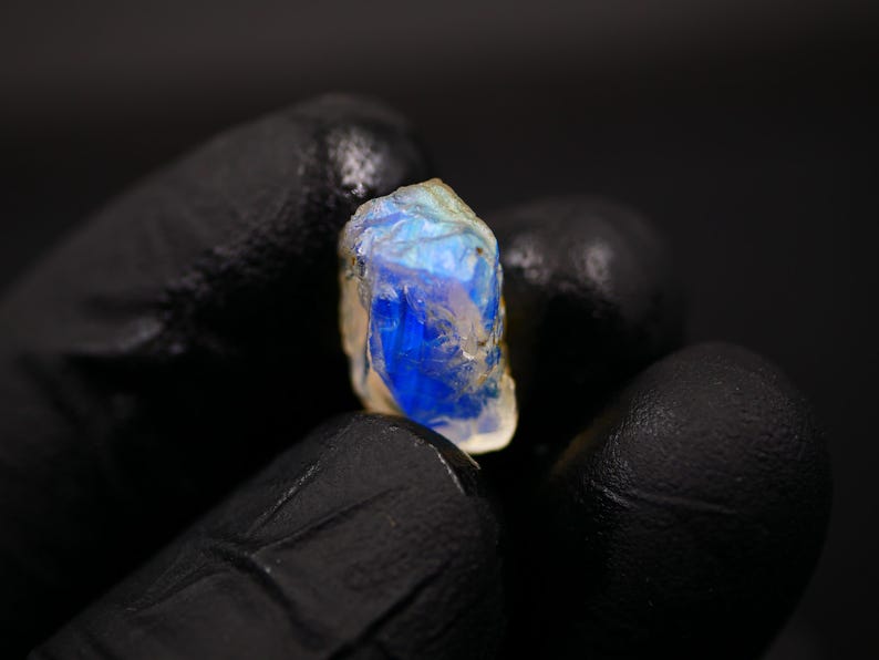 May include: A raw, uncut gemstone with a vibrant blue and white color. The stone is held against a dark background, showcasing its natural, irregular shape and unique color variations. This gemstone is a beautiful example of natural mineral formations.