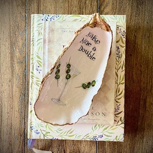 May include: A white ceramic oyster shell dish with gold trim. The dish has a green olive design and the text "Make Mine a Double" written on it.
