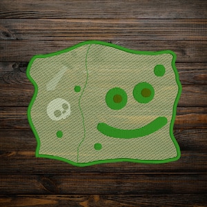 May include: Green embroidered patch with a smiling face and a skull design. The patch has a textured, woven look.
