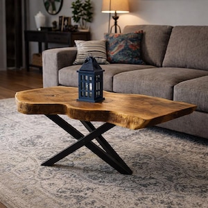 May include: A live edge wooden coffee table with black metal legs. A small, dark blue lantern sits on the table's surface. The table is in a living room setting with a gray sofa and patterned rug.