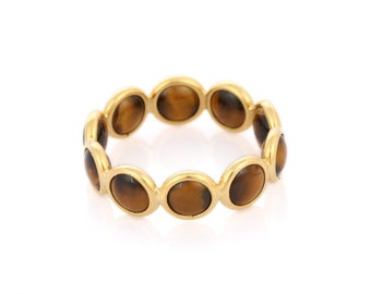 May include: A gold-colored ring featuring a series of oval-shaped tiger's eye stones. The stones are a warm brown color, set in individual gold bezels that form a continuous band. The ring is a simple yet elegant piece of jewelry.