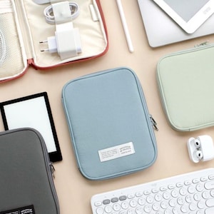 May include: Four zippered pouches in different colors, including gray, blue, green, and red, with a white keyboard and a white stylus pen. The pouches are made of a soft, textured fabric and have a zipper closure. The pouches are ideal for storing small electronics, such as a phone, charger, or headphones.